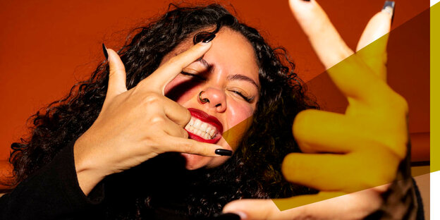 Eine Frau, rote Lippen, lockige Haare, braune Haut, Nasenring und lange schwarze Nägel. Sie zeigt mit beiden Händen das Zeichen für Rock n Roll (Mittel- und Ringfinger eingeknickt, die anderen erhoben).