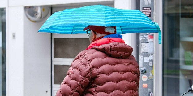 Ein Senior geht mit Regenschirm spazieren.