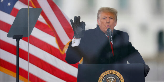 Donald Trump steht vor einer US-Fahne an einem Rednerpult
