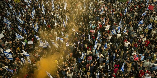 Eine Menschenmenge mit israelischen Fahnen, darüber gelber Rauch